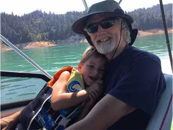 Rodney O. Hardcastle and a kid wearing a life vest in the shade on a bot on a clear lake