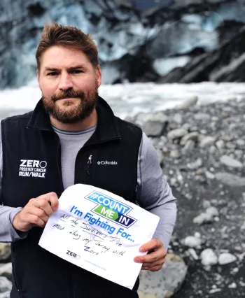 Man looking at the camera in an artic tundra holding up a reasons I fight sign