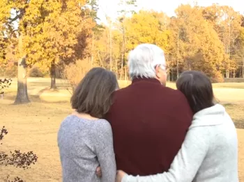A man embraced in a hug by two women looking at the trees questioning his risk of cancer