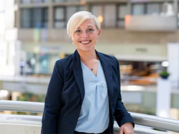 Blonde woman with very short hair wearing a light blue shirt and dark blue blazer