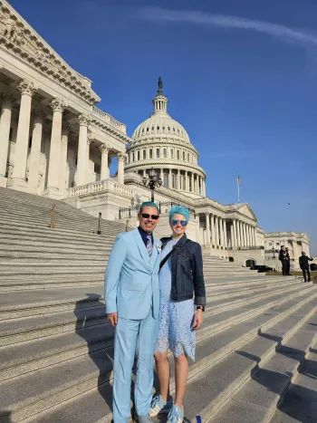 Man in powder blue suit with blue hair next to a woman in blue skirt and top also with blue hair standing on steps outside Capitol building