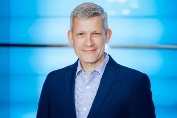 A white man with gray hair wearing a blue suit against a blue background