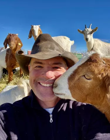 Cowboy Max and a goat kissing him on the cheek