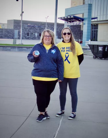 A woman wearing a blue t-shirt and a woman wearing a yellow t-shirt posing in front of the camera