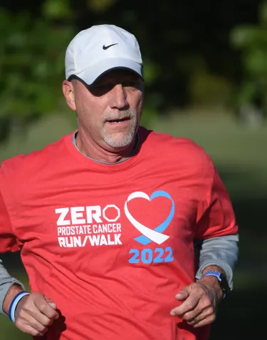 A male runner wearing a red t-shirt and a white basebal hat