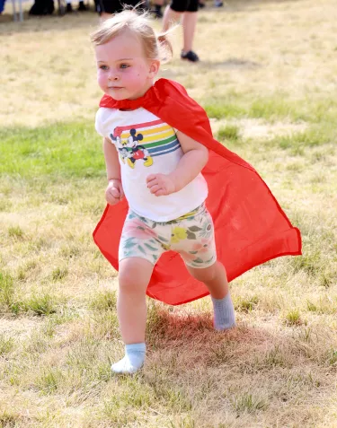 A little blond girl wearing a superhero's red cape