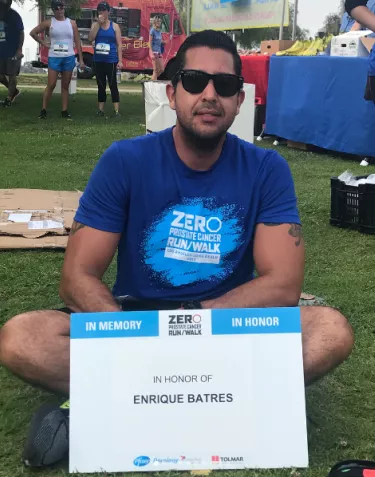 A man sitting on a lawn with a ZERO sign in front of him