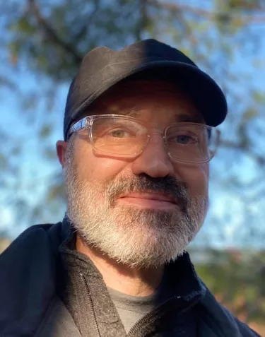 A man with grey beard wearing glasses and a baseball hat