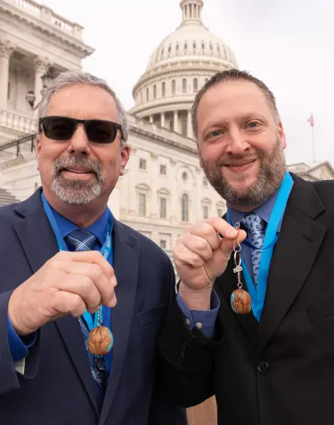Two men in suits showing walnuts in front of the Capitol