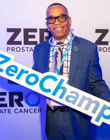 African American man in a suit holding a ZERO Champion sign