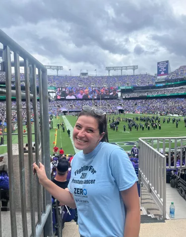 Chapter Manager, Lishey Dent, standing on stairs in the stands of the Baltimore Ravens football stadium with the field in the background