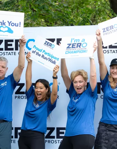 A group of four people (one man and three women) standing in front of the step-and-repeat and holding up signs supporting ZERO