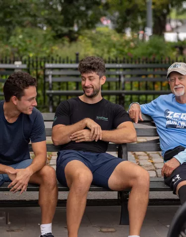 A group of three men sitting on a bench together at the 2023 Run/Walk in New York City