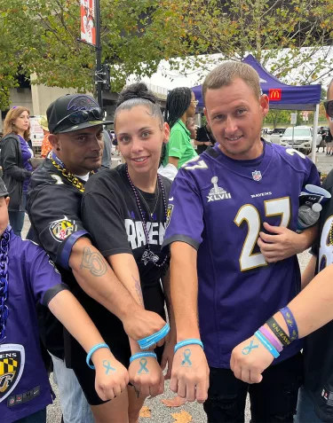 A group of Baltimore Ravens fans holding out the blue wristbands and temporary prostate cancer ribbon tattoos on their hands given out at the RavensWalk community event in 2023