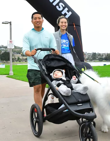 A man and woman walking under the inflatable arch while pushing a stroller and walking a Samoyed dog at the San Diego Run/Walk 2023