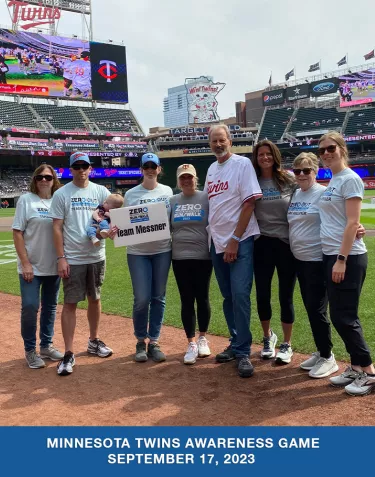 A group of people with ZERO shirts and signs standing on the field of the Minnesota Twins baseball stadium