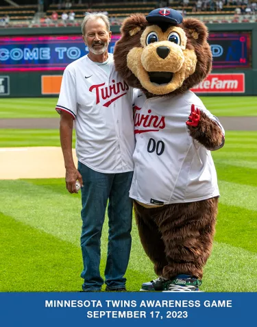 A man wearing a Minnesota Twins jersey standing with the mascot on the field