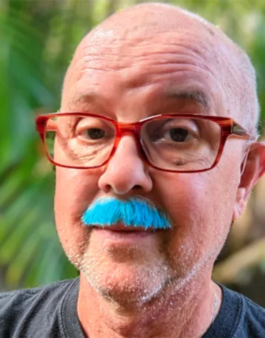 A senior man with red rimmed glasses and a blue mustache