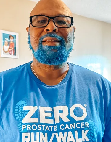 A Black man with rectangular glasses and a beard dyed blue