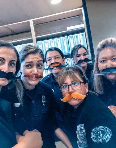 A group of female police officers wearing paper mustaches for Grow & Give