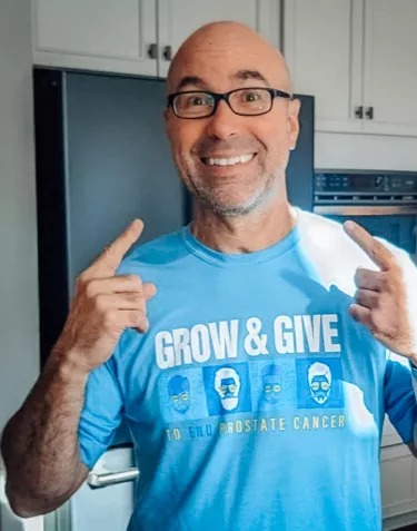 A bald man wearing rectangular glasses and a Grow & Give tshirt