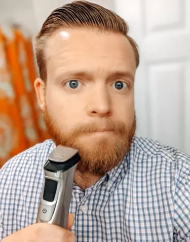 A young man with red hair holding a razor up to his beard