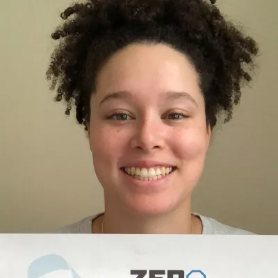 Young woman with curly hair smiling and holding a ZERO sign