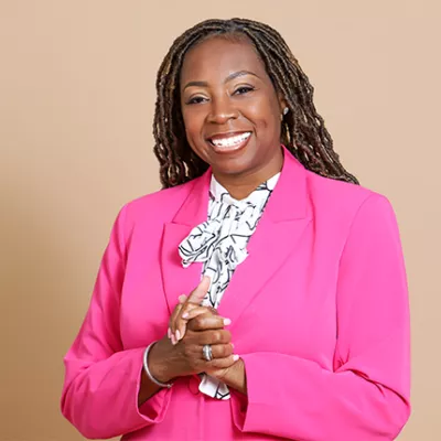 A Black woman wearing a hot pink blazer smiling and clasping her hands together