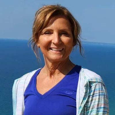 A woman standing in front of an ocean wearing a blue nike shirt and a striped sports jacket