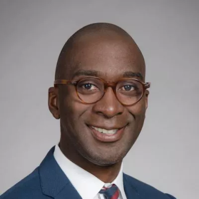 A Black man wearing a suit and glasses, posing for his headshot