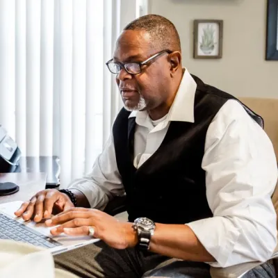 A man sits at a table with his laptop open, tuning into a virtual education session.