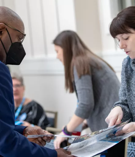 A woman with blue hair highlights sharing reading materials with an African American man in a suit