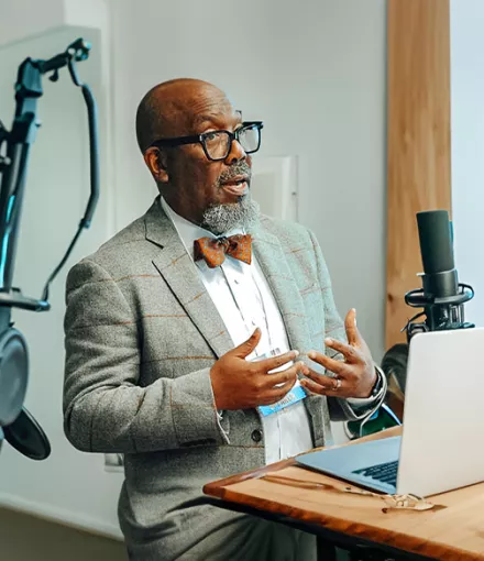 Dr. Reggie Tucker-Seely in front of a computer and microphones 