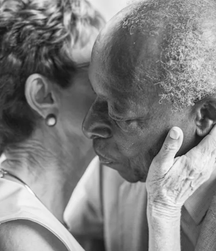 A black and white photo of a senior couple having an intimate moment as she kisses his cheek