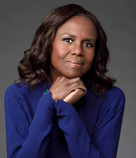 A black woman wearing a blue shirt holding her hands under her chin