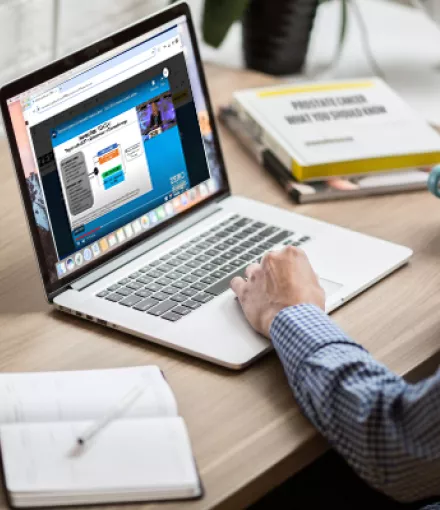 A Black man offscreen looking at a laptop with the virtual summit pulled up on a web browser