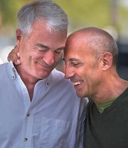 Two older men smiling with their heads pressed together 