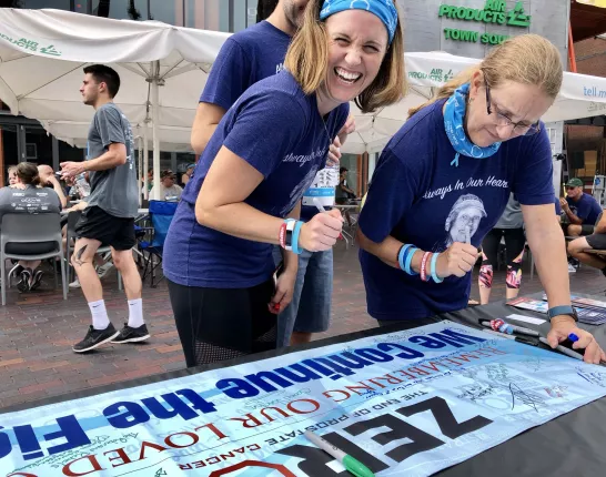 Two women wearing memorial shirts sign a remembrance banner for ZERO