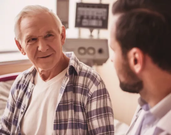 A male patient sitting on a hospital bed speaking with his doctor