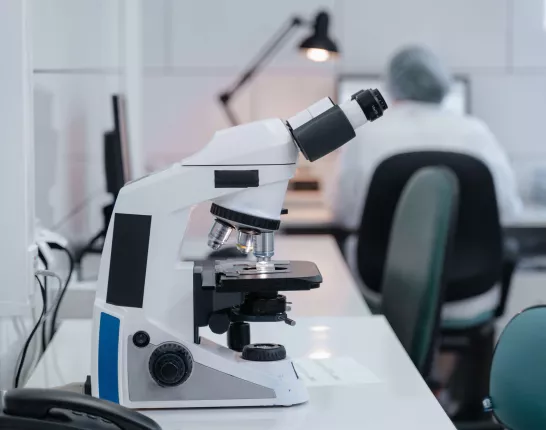 Microsope in focus while scientist works in background in lab