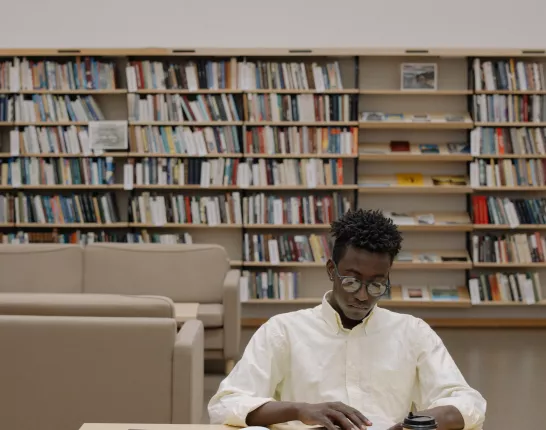 Black Man in White Dress Shirt Sitting on White Chair in the library