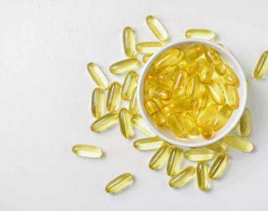 white bowl of yellow pill capsules overfilled onto white background