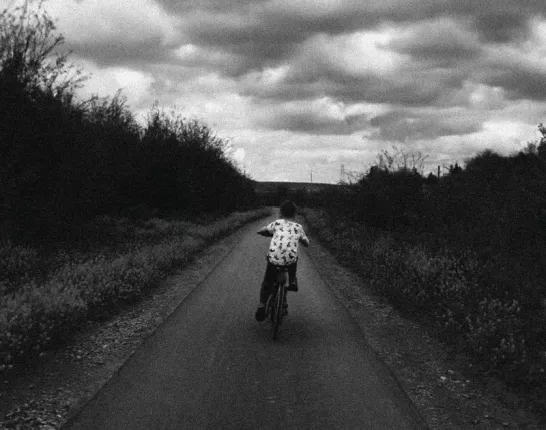 Album art of a kid bicycle racing down a rural road in black in white