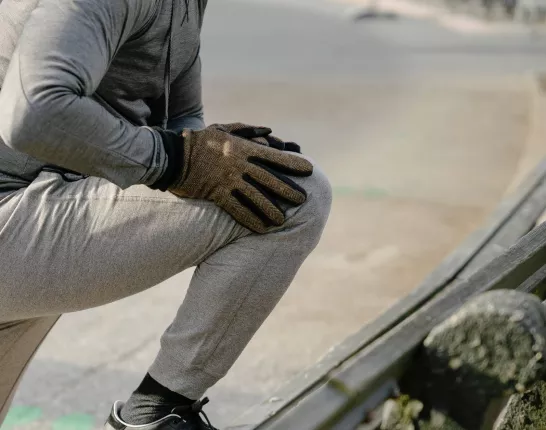 A man in cold weather jogging attire stretching on the side of the road