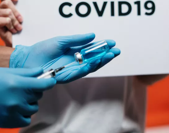 Person in gloves Holding Syringe in front of Covid19 sign