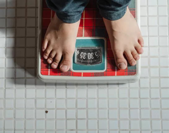 Crop kid weighing on red scale