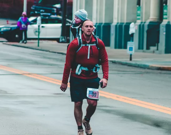 Man Carrying Baby at Back While Walking Near Buildings