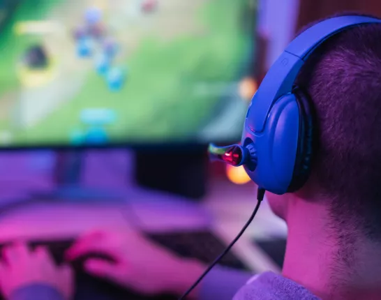 A man playing League of Legends on a colorful lit up back-lit desk wearing a blue headset