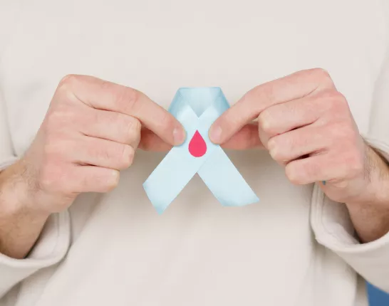 An individual in a white top holding a blue ribbon with a blood drop