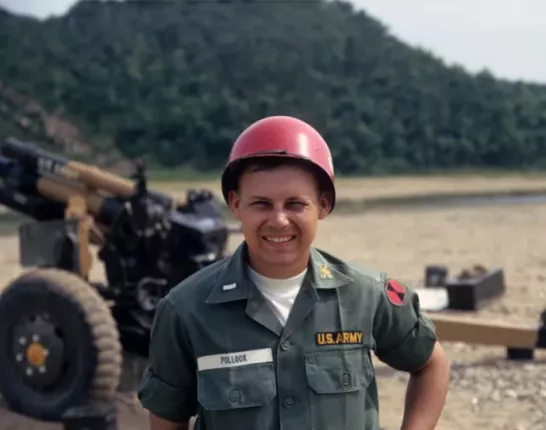 Us. Army man in uniform with red helmet standing in front of a M102 105mm towed wowitzer